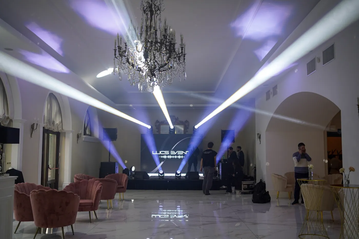 Salone con lampadario e fasci bianchi a ventaglio, logo riflesso sul marmo