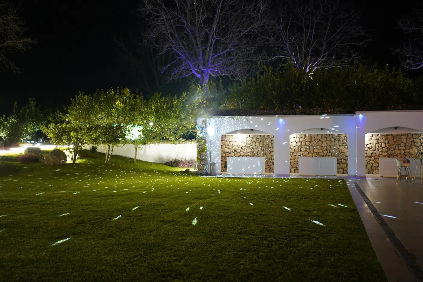 Giardino di notte con le luci a puntini sul prato e sul muro ad archi