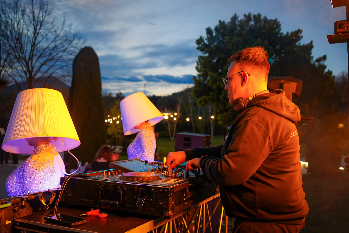 DJ alla console all’aperto, al tramonto, con due performer dietro