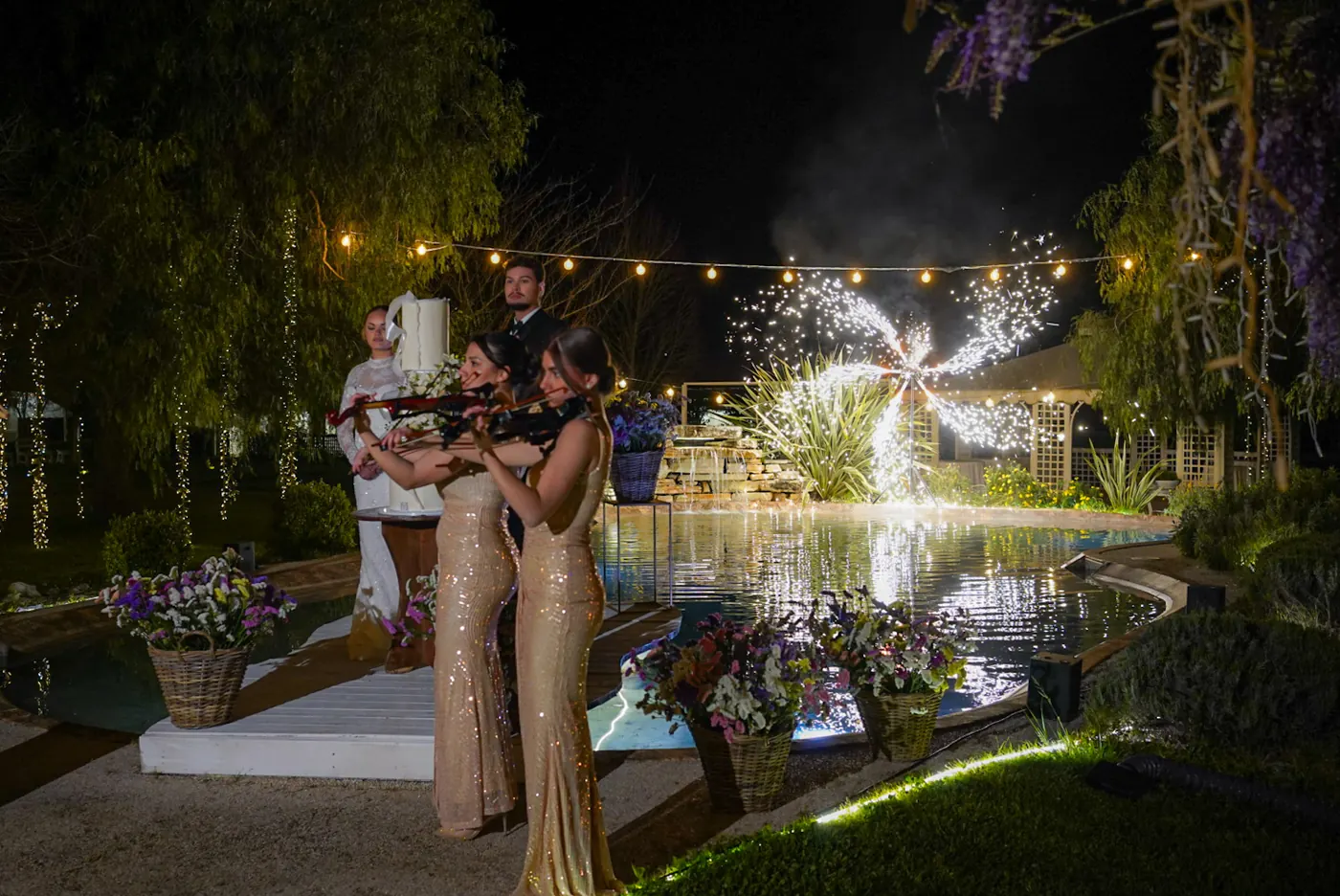 Due violiniste in abito dorato suonano a bordo piscina, di notte, con le fontane fredde accese dietro