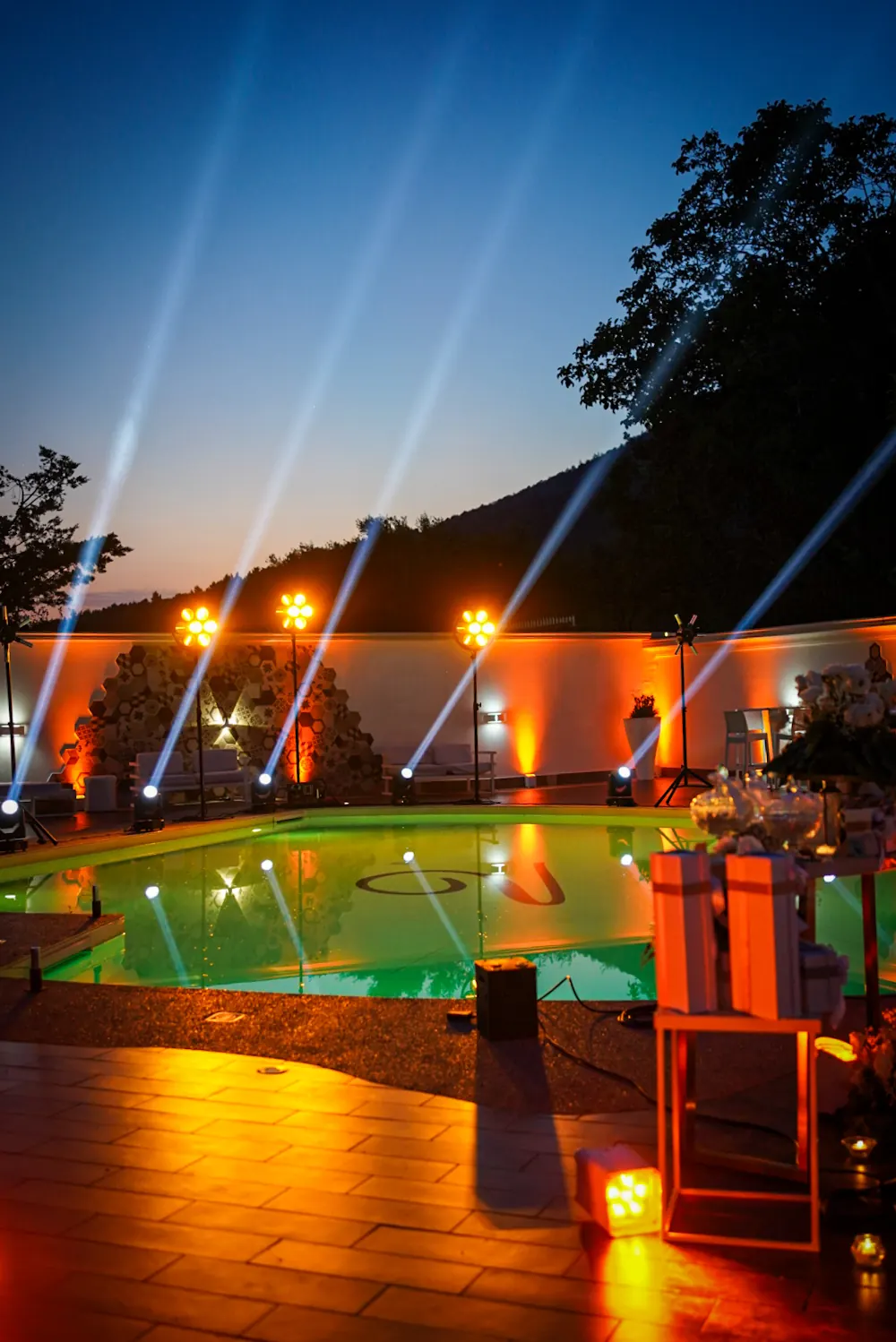 Teste mobili a bordo piscina che sparano fasci di luce verso il cielo, al tramonto